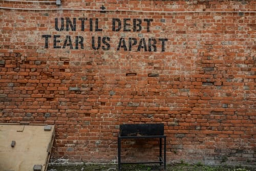 Image of a brick wall with the words "until debt tear us apart" painted