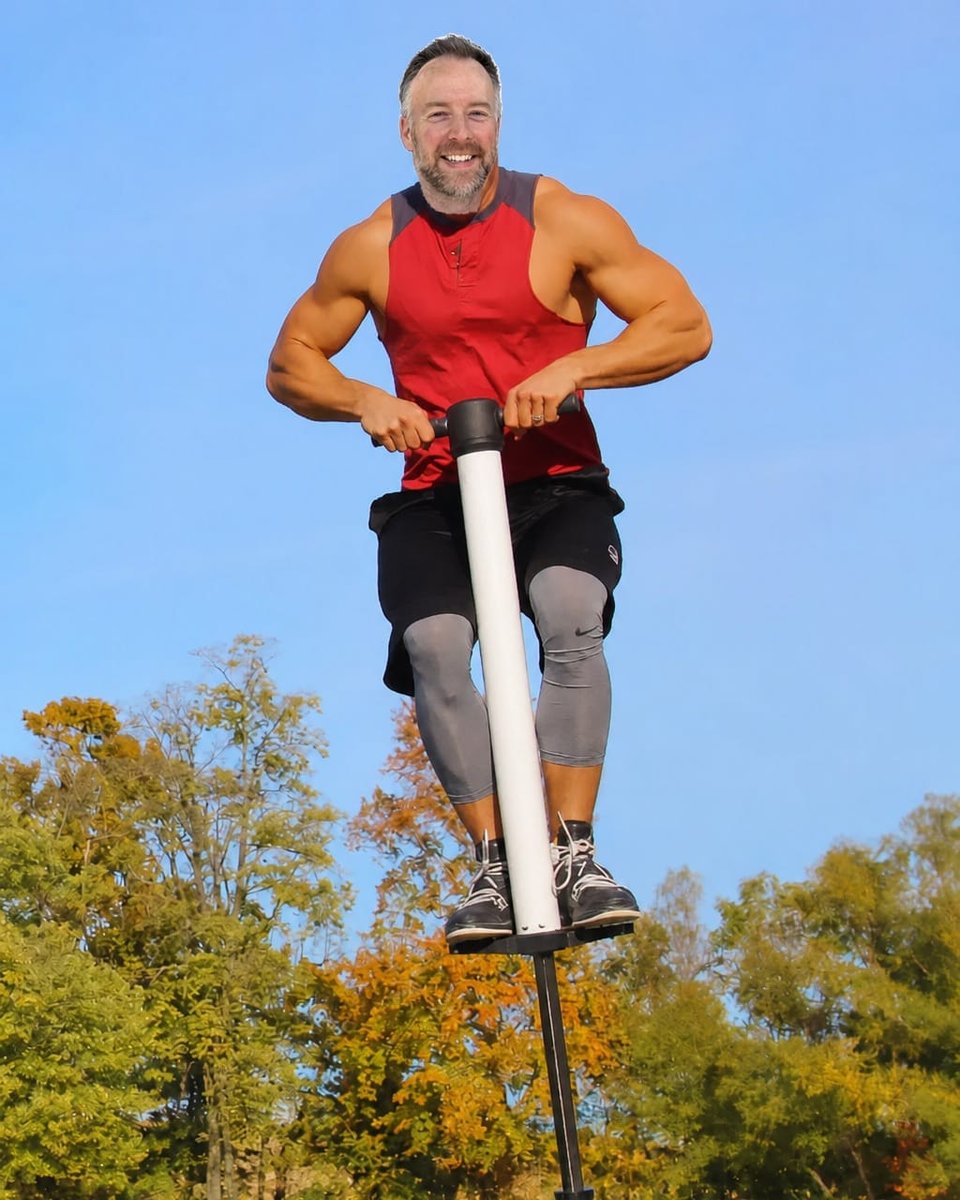 A man with an intentionally pasted-on face jumps on a white pogo stick above a park.