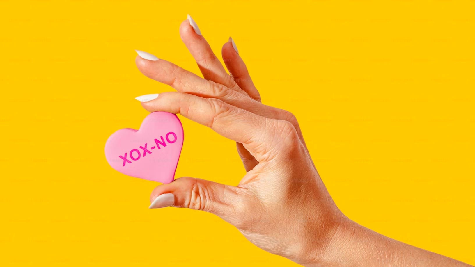 A woman's hand holding a heart-shaped Valentine's cookie that reads "xox-no"
